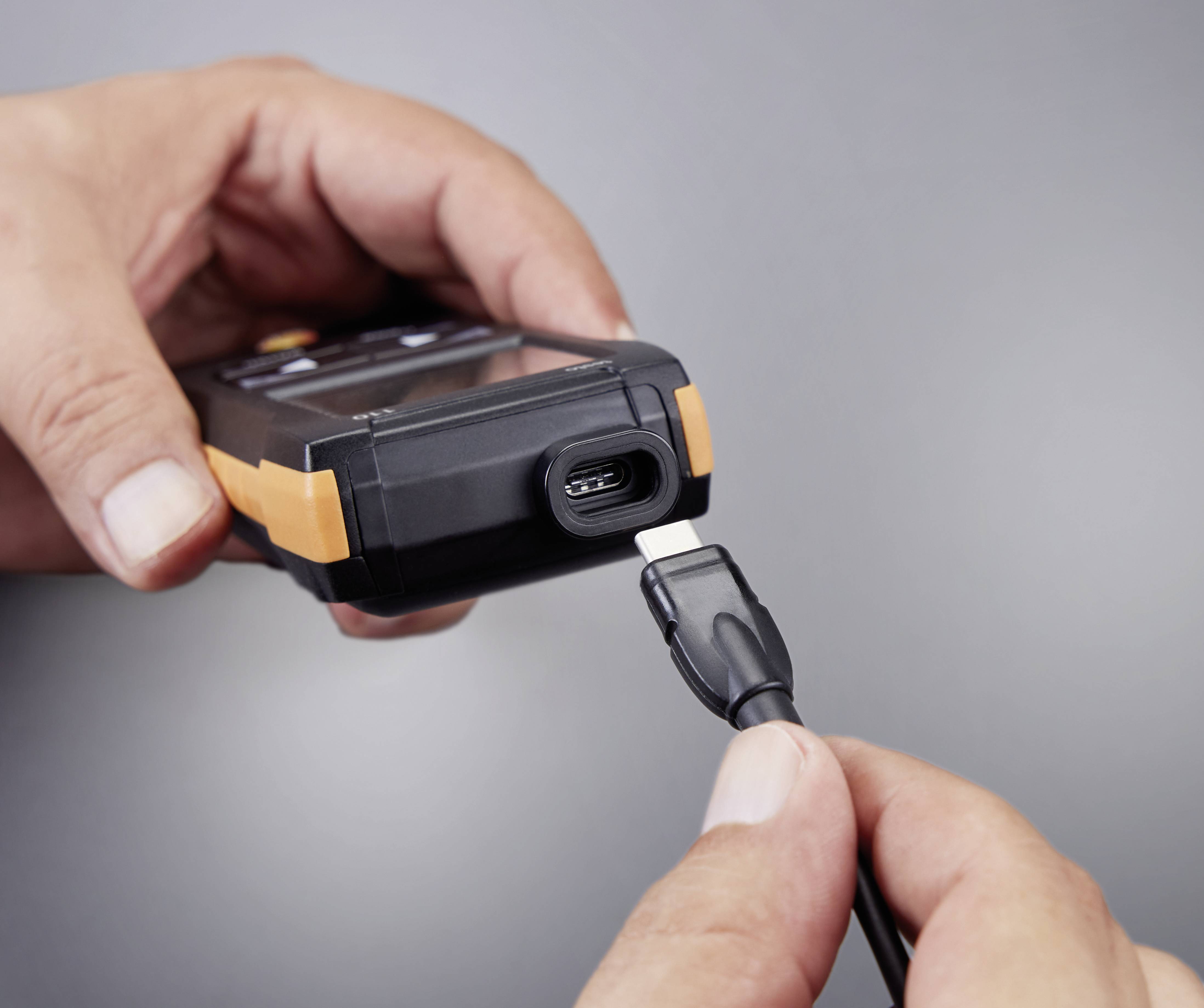 Een hand houdt een apparaat met een USB-C-aansluiting vast, terwijl een andere hand een USB-C-kabel insteekt om verbinding te maken.