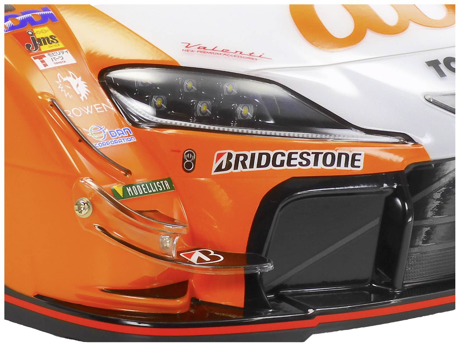 Close-up van de voorbumper van een racewagen met sponsorlogo's, waaronder Bridgestone. De foto toont details van de koplampen en het design.