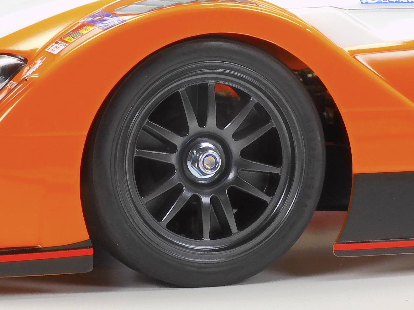 Close-up van een zwart racewagenwiel met een oranje spatbord, benadrukt snelheid en sportiviteit.