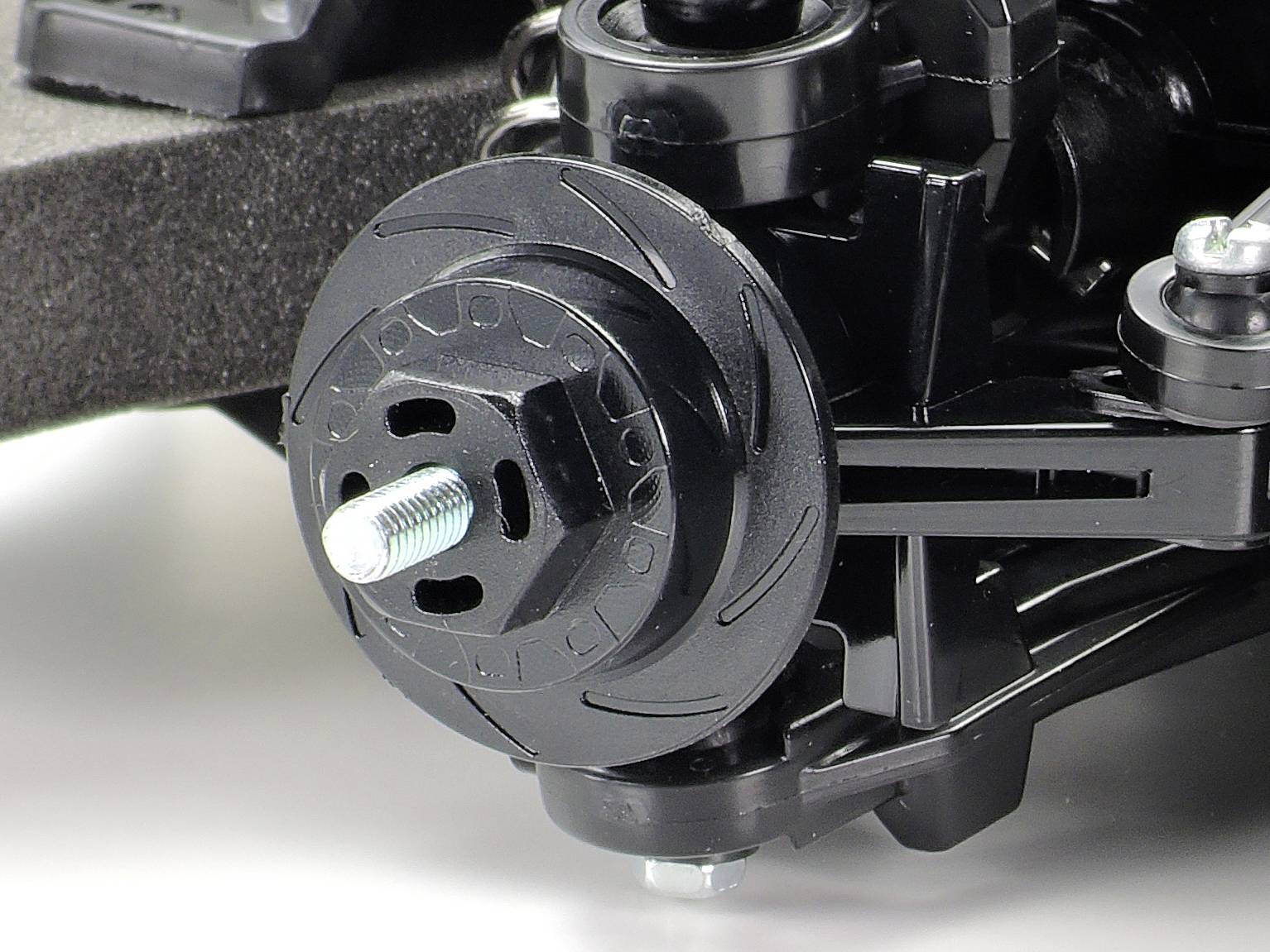 Close-up van een zwart modelautoonderdeel met zichtbare schroef en wielophanging. Focus op technische details en verbindingen.