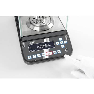 Een elektronische weegschaal toont op het display '0,00000 g'. Een gehandschoende hand drukt op een knop aan de voorkant van de weegschaal.