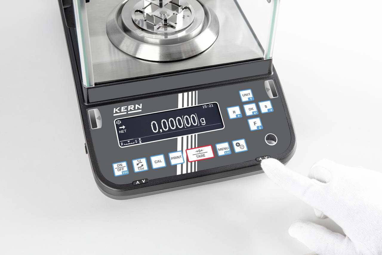 Een elektronische precisieweegschaal met digitaal display toont '0,00000 g'. Een gehandschoende hand raakt een knop aan.