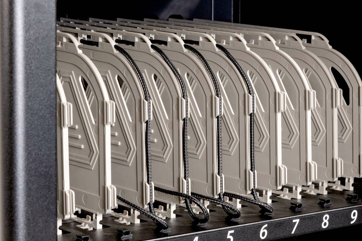 Oplaadstation met genummerde aansluitingen voor elektronische apparaten, witte laadadaptersleuven en zwart-witte oplaadkabels.