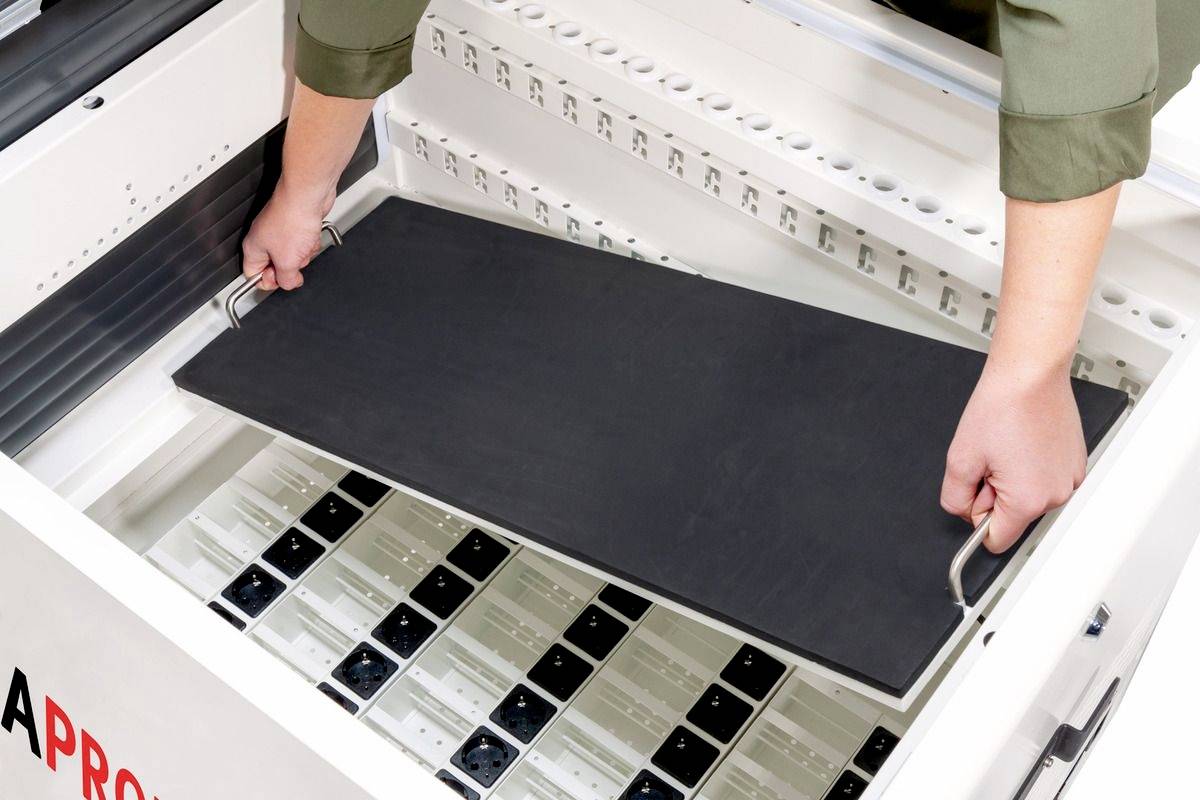 Een persoon tilt een zwart paneel uit een lade met stopcontacten. De scène wijst op een technische of elektronische omgeving.