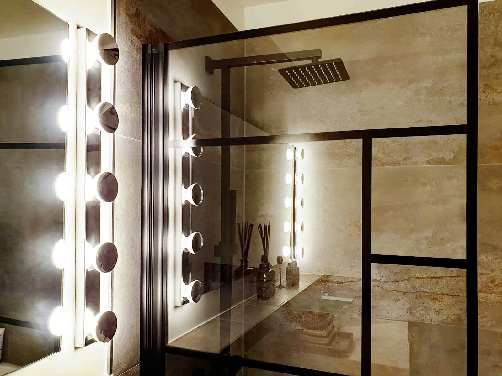 Een modern badkamer met een spiegelwand, helder verlicht door zijdelingse lampen. Een glazen douche is eveneens zichtbaar.