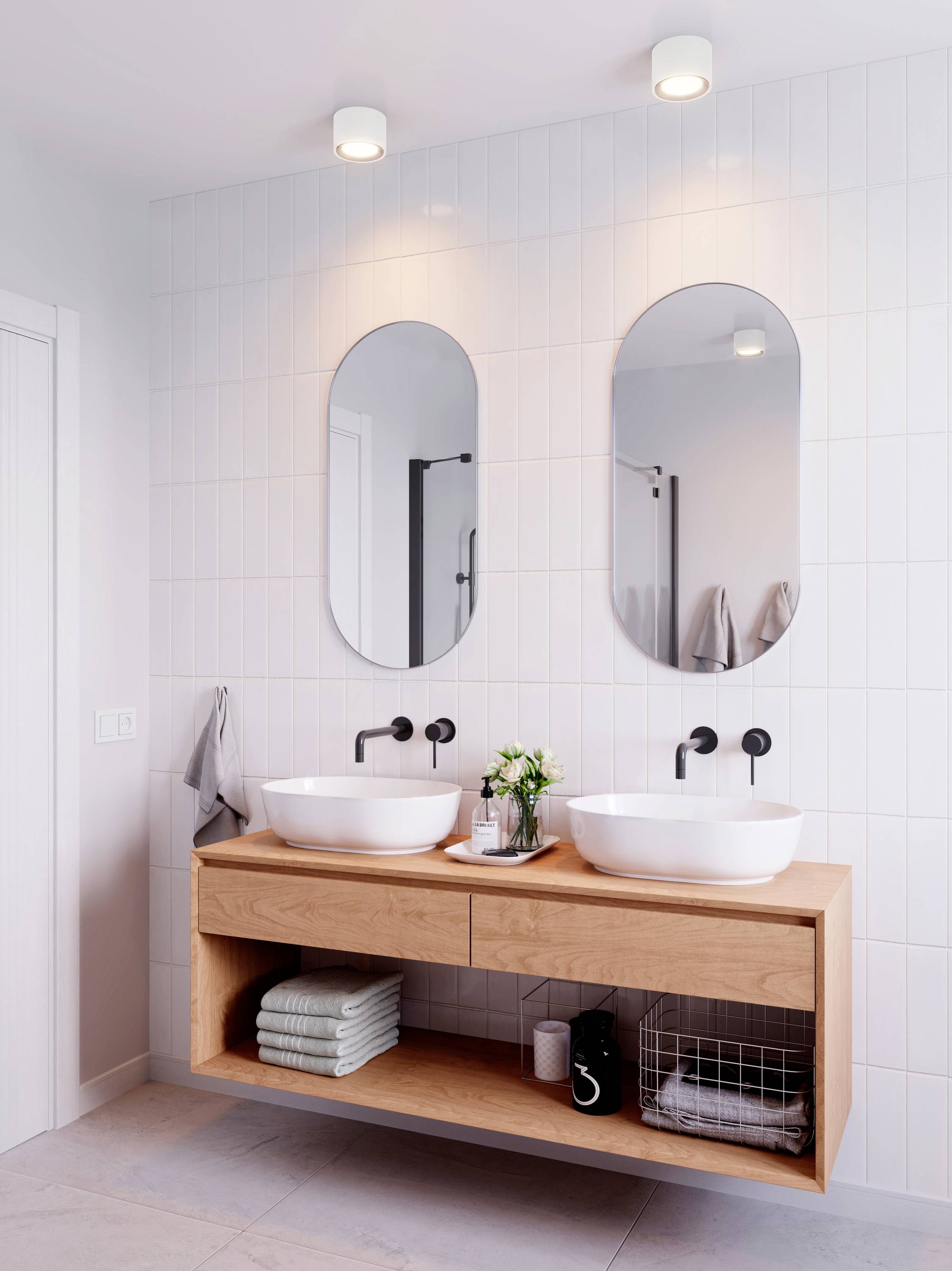 Een modern badkamerinterieur met twee ovale spiegels boven witte wastafels op een houten onderkast. Handdoeken en planten decoreren de ruimte.