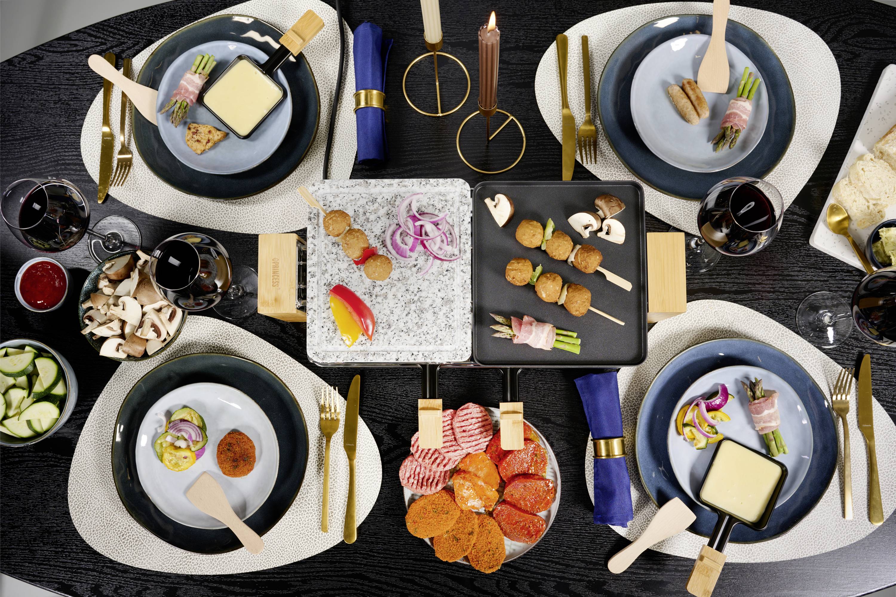 Een gedekte tafel met verschillende tapas: kaas, brood, groenten en vleesgerechten. Glazen met rode wijn en blauw gevouwen servetten.