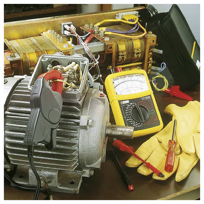 Een elektromotor en een multimeter op een werkbank, omringd door gereedschappen en kabels.
