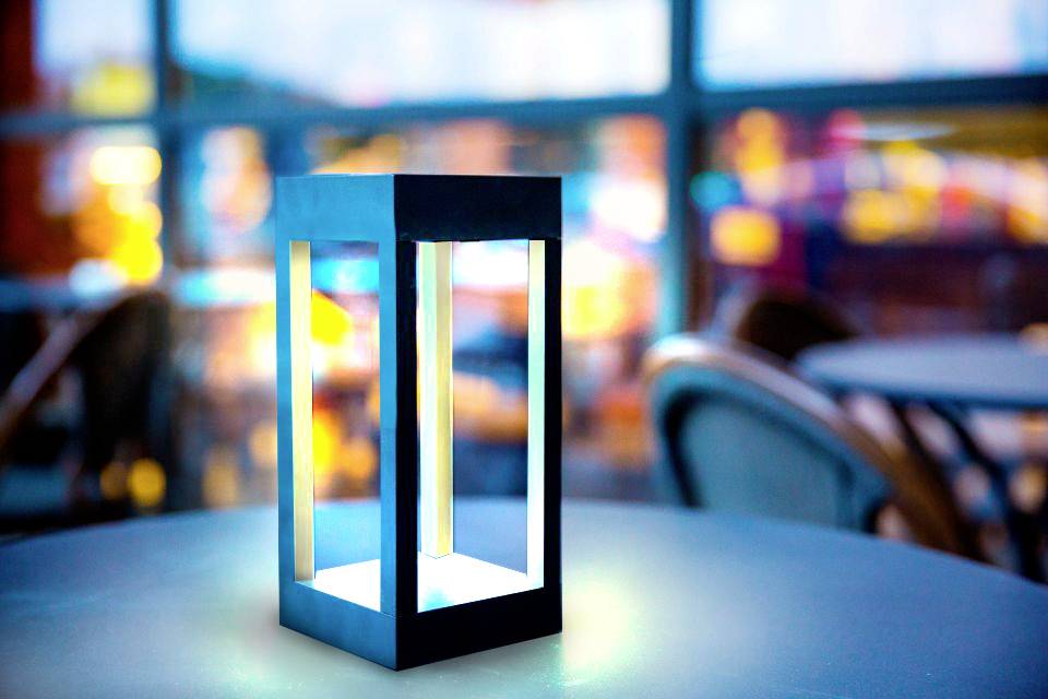 Een moderne, stralende tafellamp staat op een tafel in een wazig, sfeervol verlicht café of restaurant.