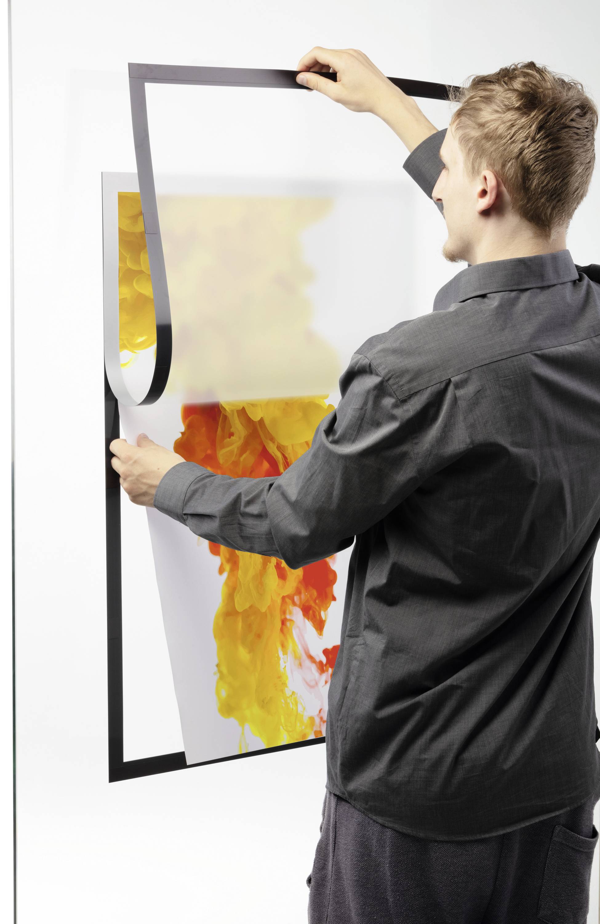 Een persoon hangt een kunstwerk met een geel en oranje motief aan de muur.