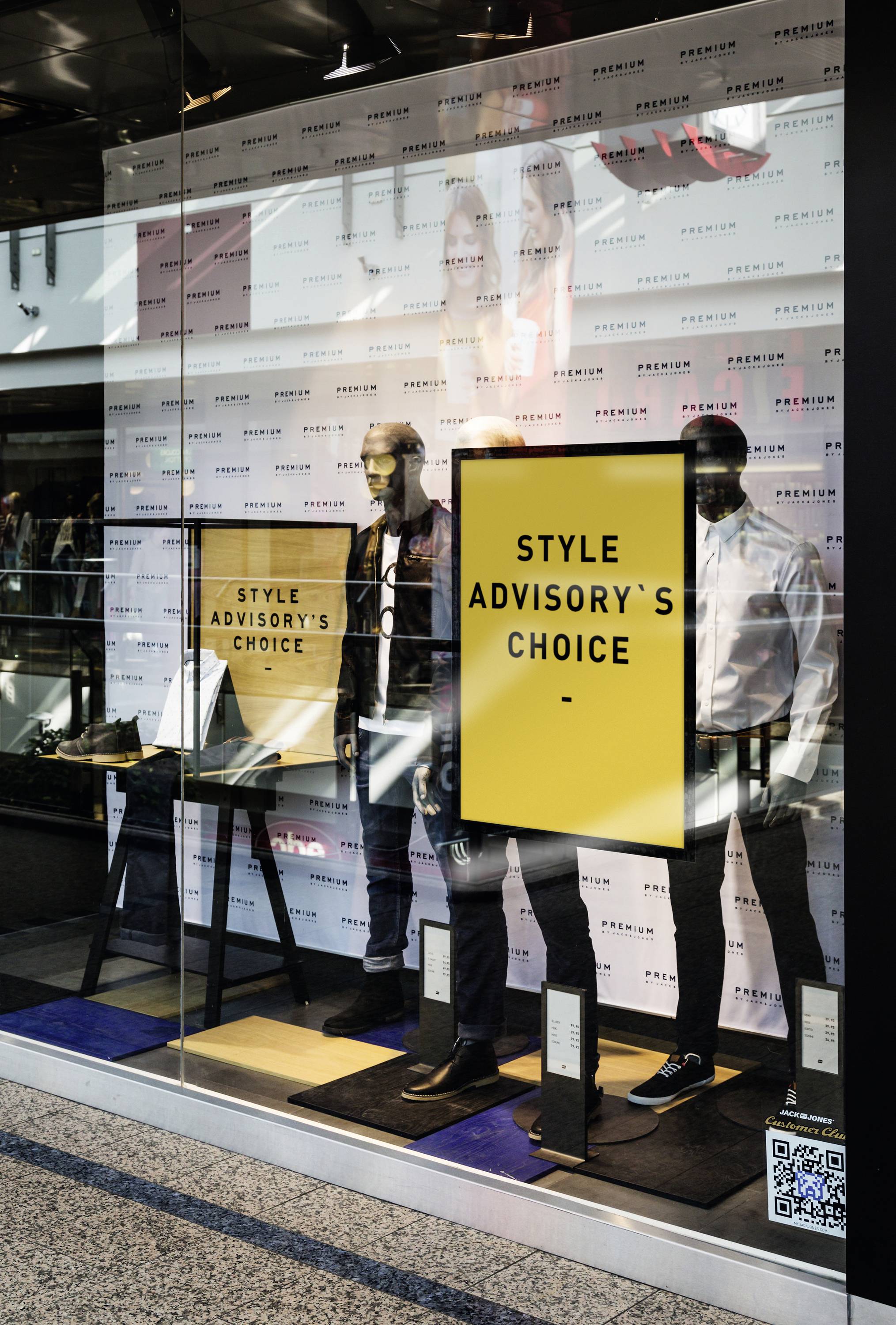 Etalage met twee etalagepoppen die modieuze herenkleding dragen. Een geel bord met de tekst 'Style Advisory's Choice'.