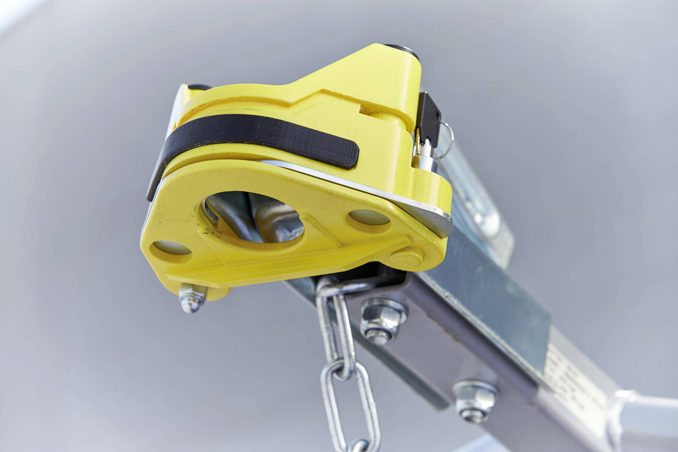 Een gele kabeltrekmechanisme met ketting aan een metalen frame, gebruikt voor het veilig optillen en zekeren van lasten.