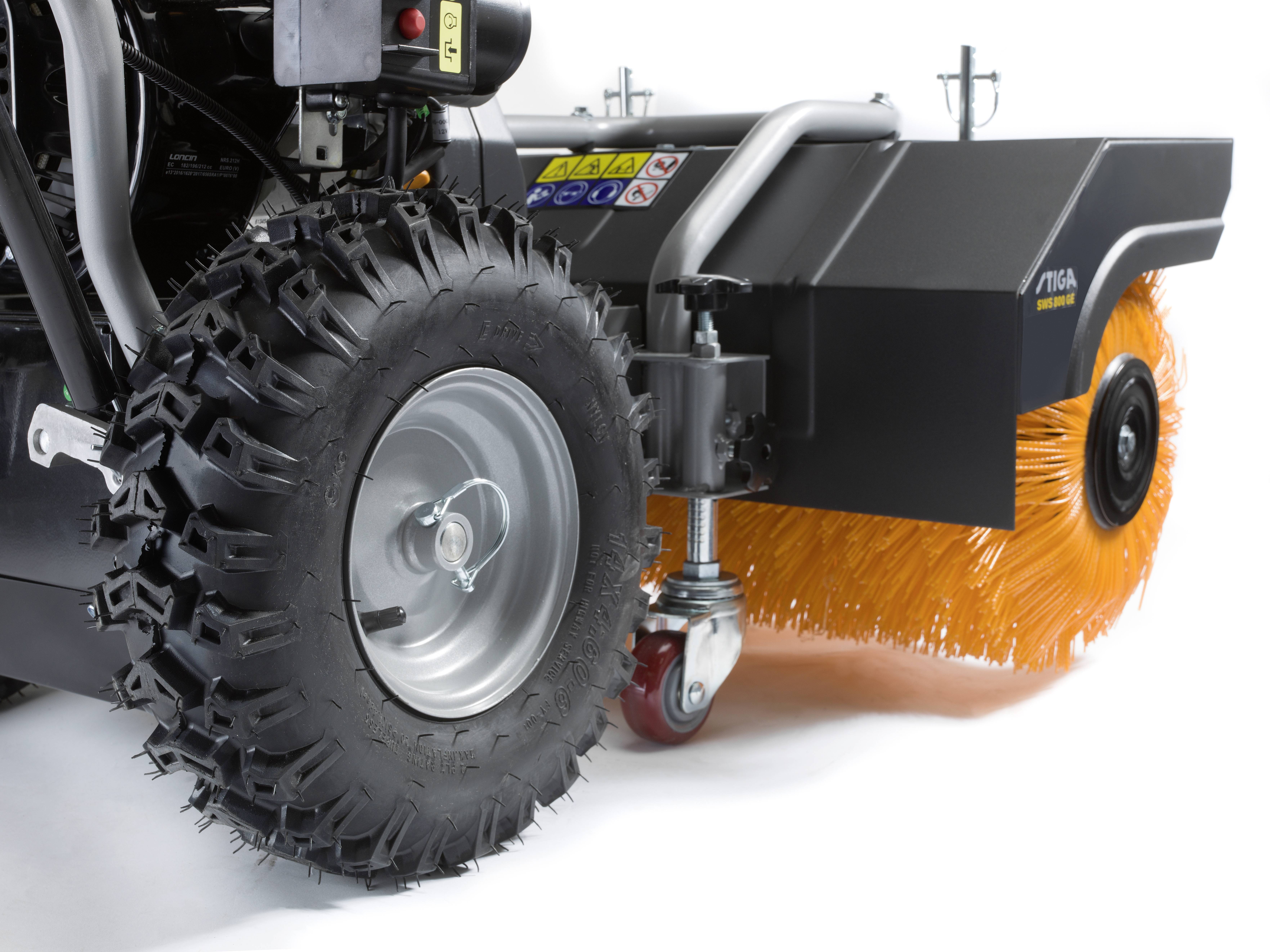 Close-up van een grasmaaier met een grote, oranje borstel aan de voorkant, geschikt voor reinigings- of sneeuwruimwerkzaamheden.