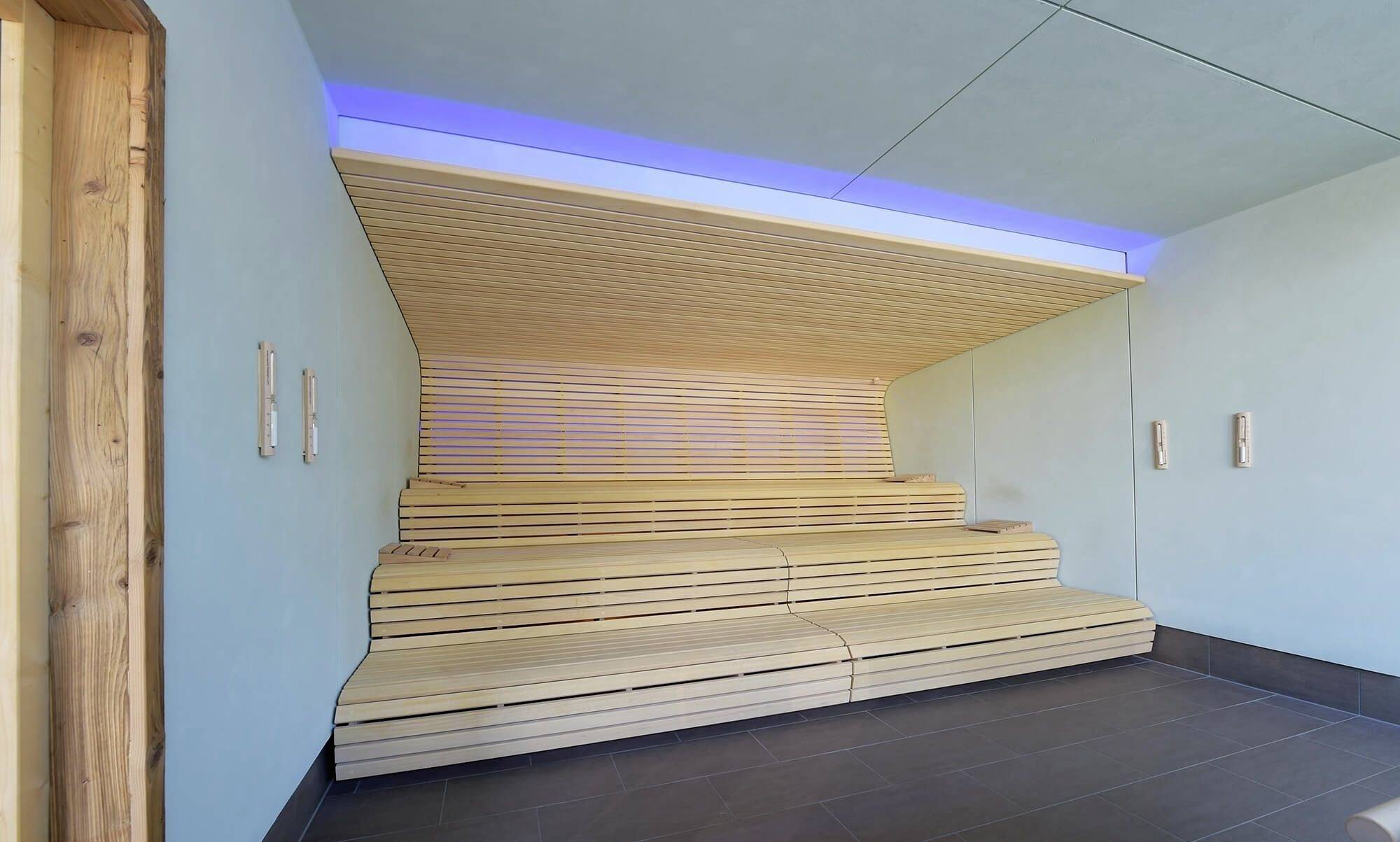 Een moderne sauna met houten betimmering en meerdere zitbanken. Blauwachtig licht verlicht de ruimte subtiel.