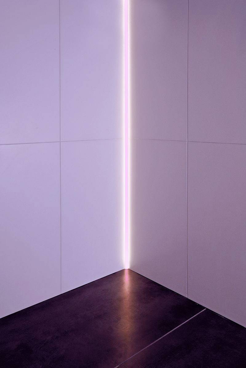 Een minimalistische hoek met een subtiele verticale neonroze lichtstreep die wordt gereflecteerd op een donkere vloer.