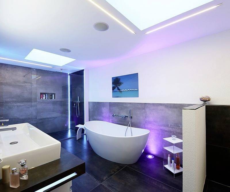 Modern badkamer met vrijstaand bad, groot wastafel en regendouche. LED-verlichting in blauw en paars.