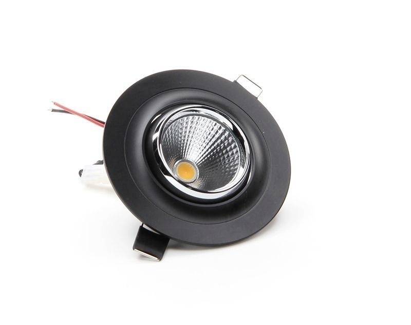 Een ronde, zwarte LED-schijnwerper met zilveren behuizing en uitstekende kabels ligt op een wit oppervlak.