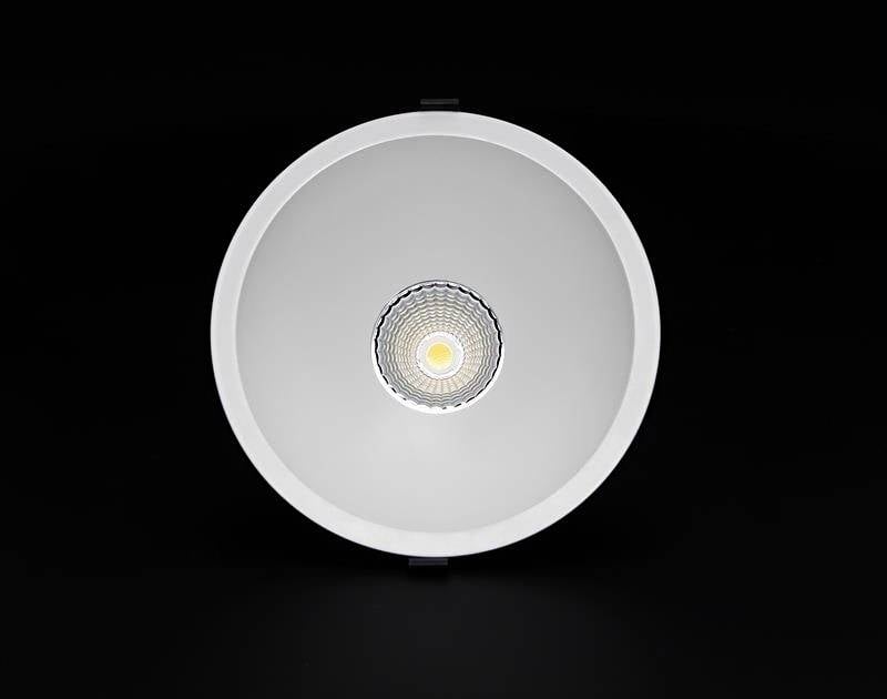 Ronde plafondlamp met metalen frame, gecentreerd in het midden, straalt warm licht uit, tegen een zwarte achtergrond.