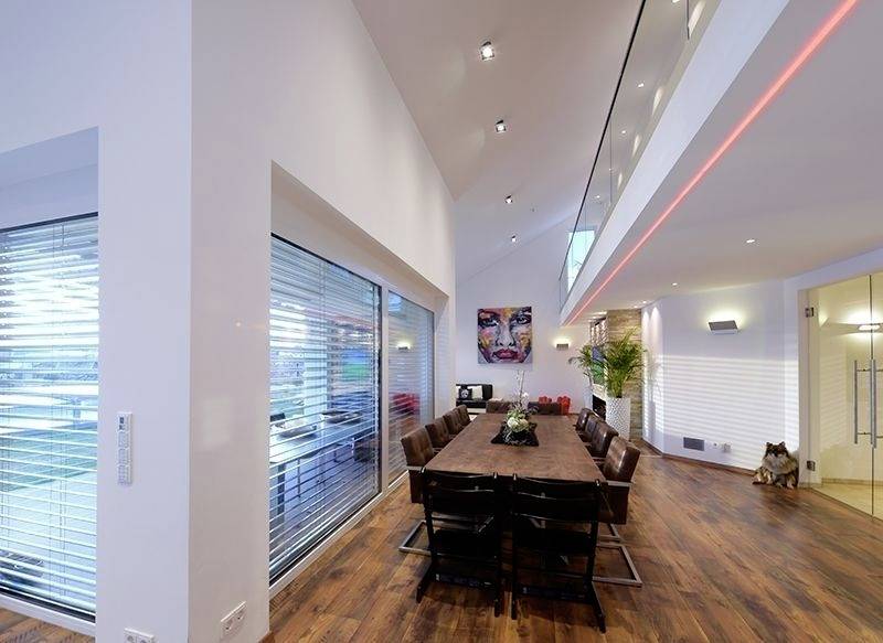 Ruimtelijke moderne eetkamer met een lange houten tafel, bruine leren stoelen, grote ramen en kunstwerken aan de muren.