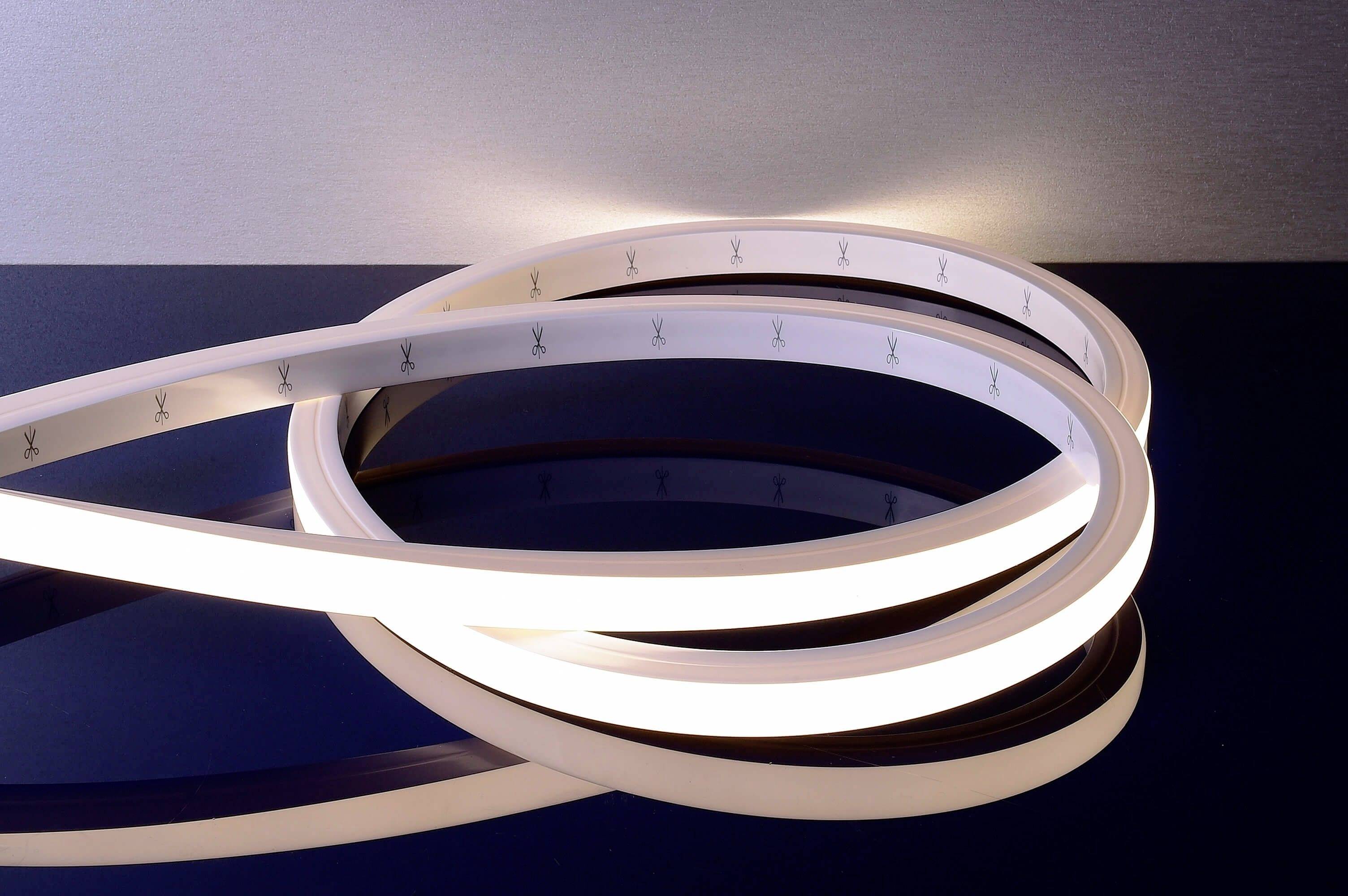 Flexibele LED-lichtstrip op donkere ondergrond. De strip is in gebogen vormen gerangschikt en verlicht de omgeving subtiel.