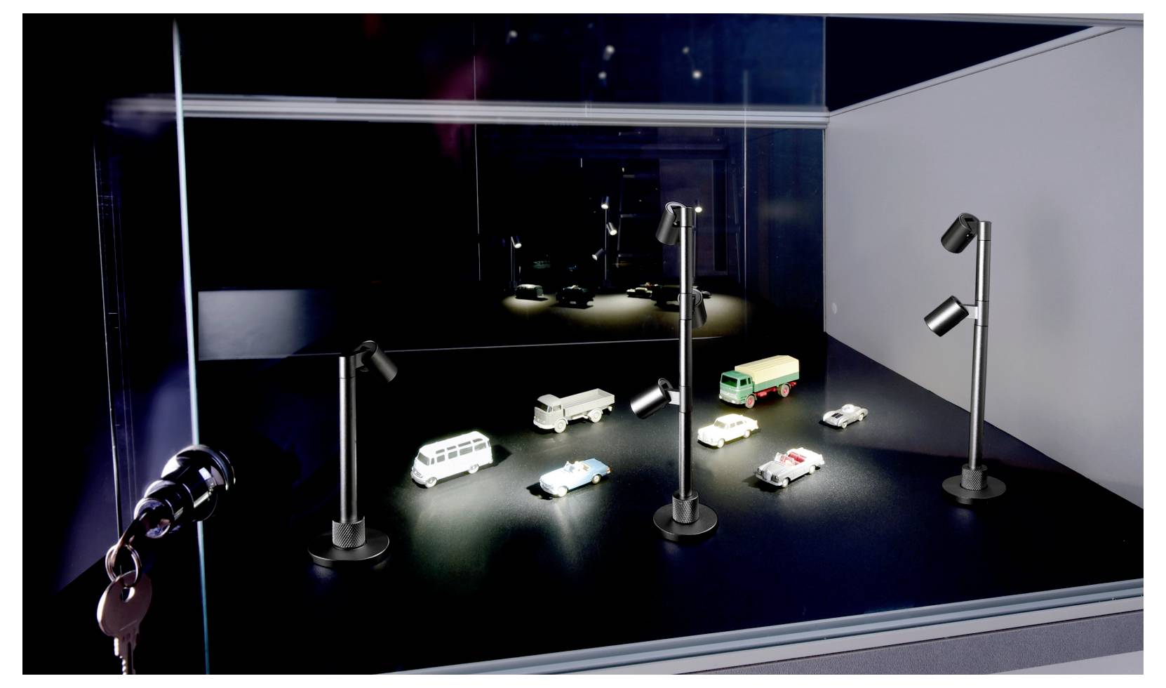 Model van een verlichte nachtelijke straatscène met verschillende kleine voertuigen op een donker presentatieplatform in een glazen vitrine.