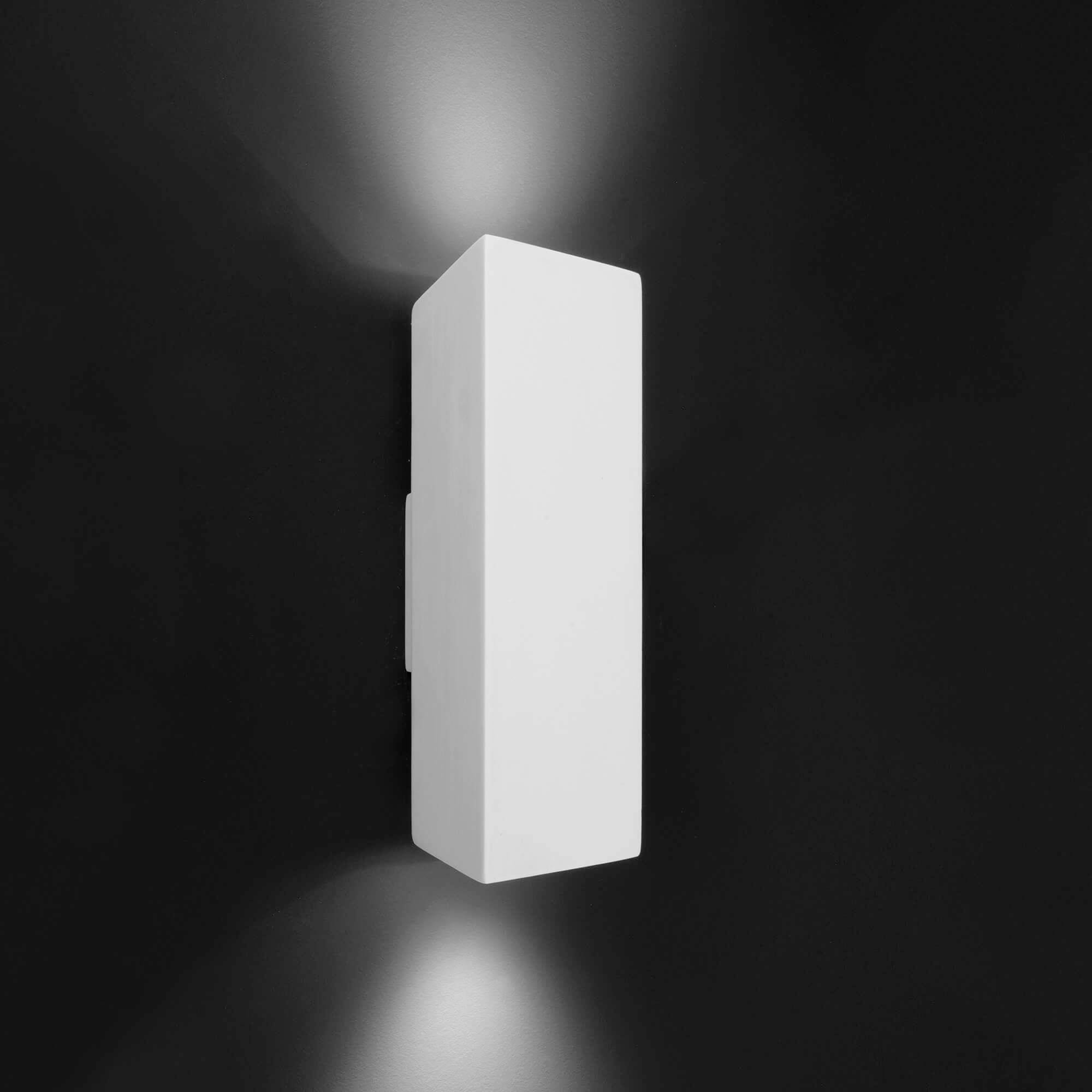 Witte, rechthoekige wandlamp op zwarte achtergrond met lichtstralen gericht naar boven en beneden.