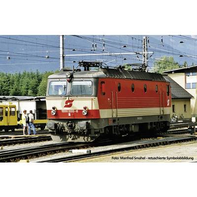 Een rode en grijze elektrische locomotief staat op een spoor van het station, omringd door andere spoorrails en gebouwen op de achtergrond.
