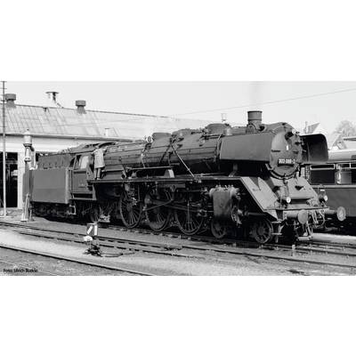 Zwart-witfoto van een stoomlocomotief op een treinstation. Een man staat op de locomotief. Op de achtergrond zijn gebouwen zichtbaar.