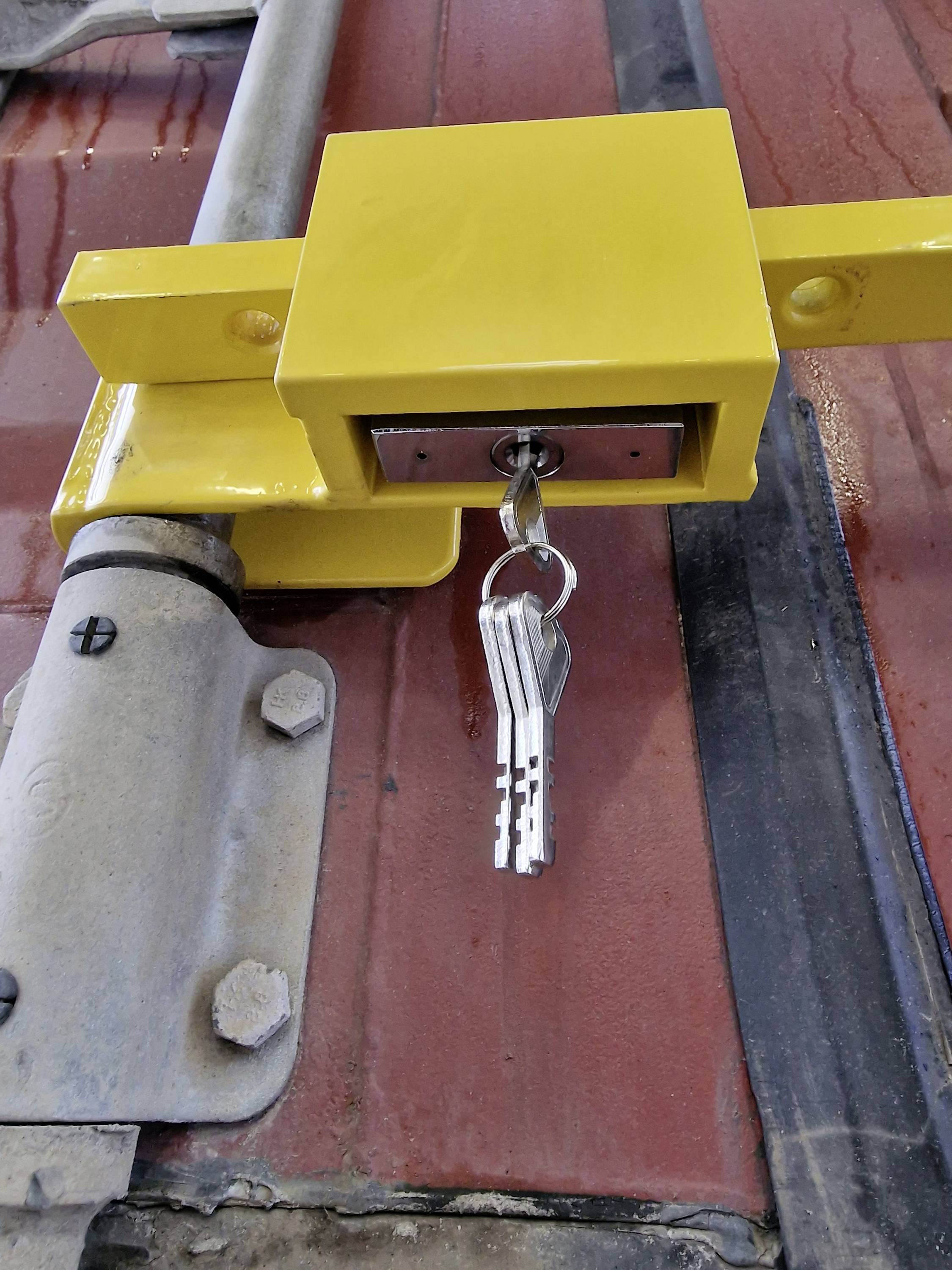 Een geel slot aan een metalen poort met steeksleutels in de lus, gemonteerd op een rode achtergrond.