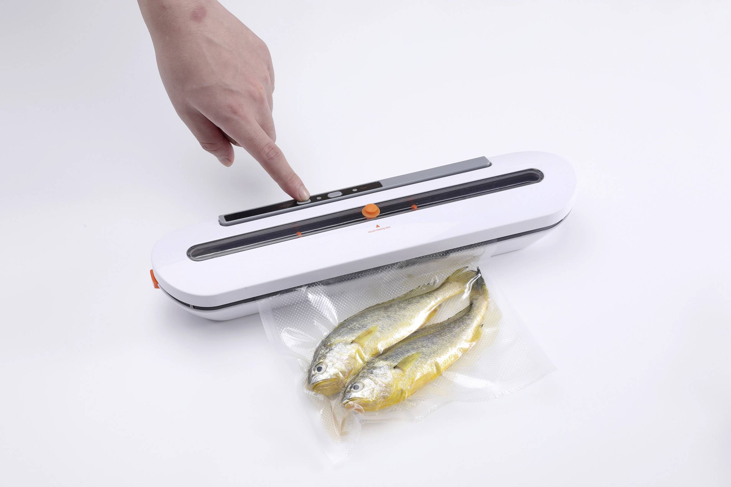 Een hand bedient een folielasapparaat dat twee vacuümverpakte vissen op een witte achtergrond verzegelt.