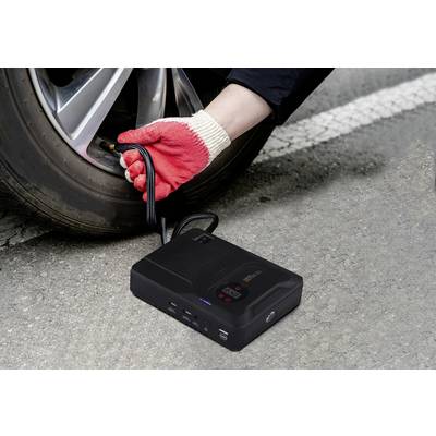 Een hand met rode handschoenen pompt lucht in een autoband met een draagbare compressor langs de weg.