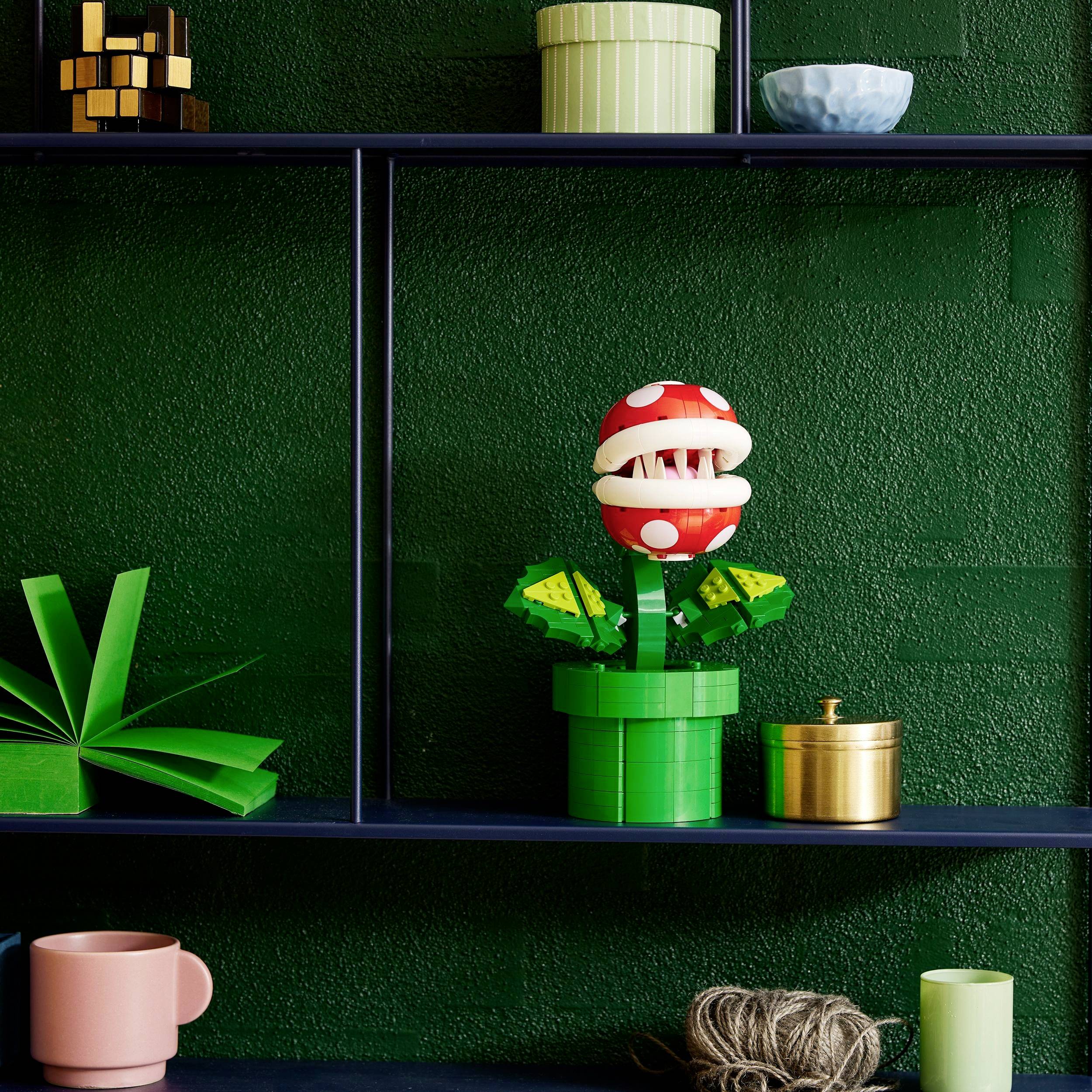 Een speelgoed van een vleesetende plant op een plank, omringd door geometrische decoraties, op een groene achtergrond.