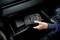 Hand legt een zwarte tas met 'OSRAM'-logo in het open dashboardkastje van de auto.