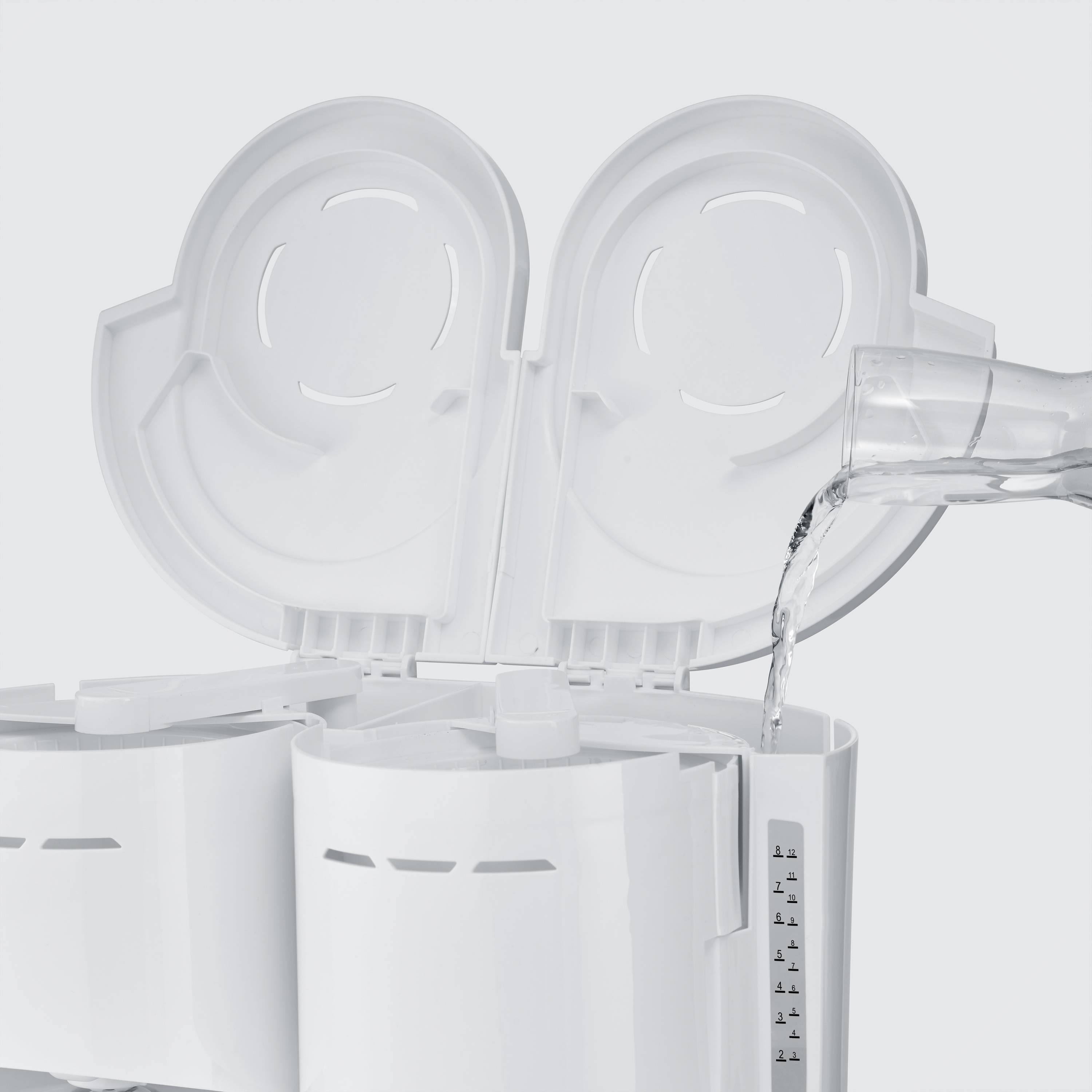 Een waterkoker met open deksel, terwijl water uit een container wordt ingeschonken. De waterstandsindicator is zichtbaar.