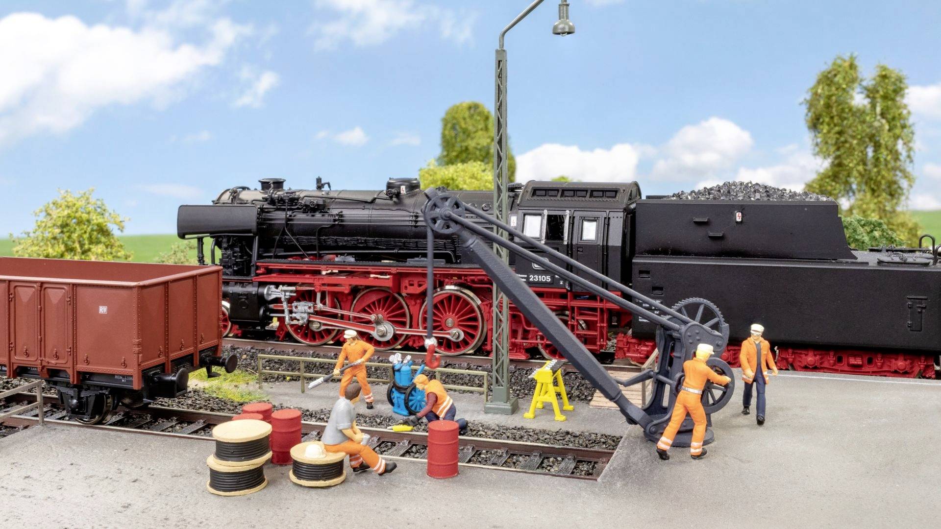 Miniatuur-spoorbaan met een stoomlocomotief, omringd door werkende figuren in oranje werkkleding die spoorwegreparaties uitvoeren.