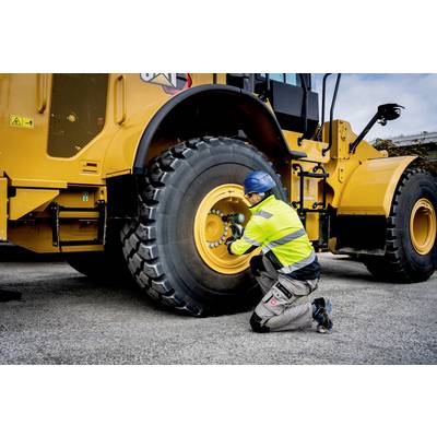 Een arbeider in beschermende kleding draait bouten vast aan een grote voertuigband op een bouwterrein.
