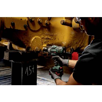 Een persoon gebruikt een groene accuboormachine om schroeven aan te draaien aan een groot, geel machinedeel in een werkplaats.