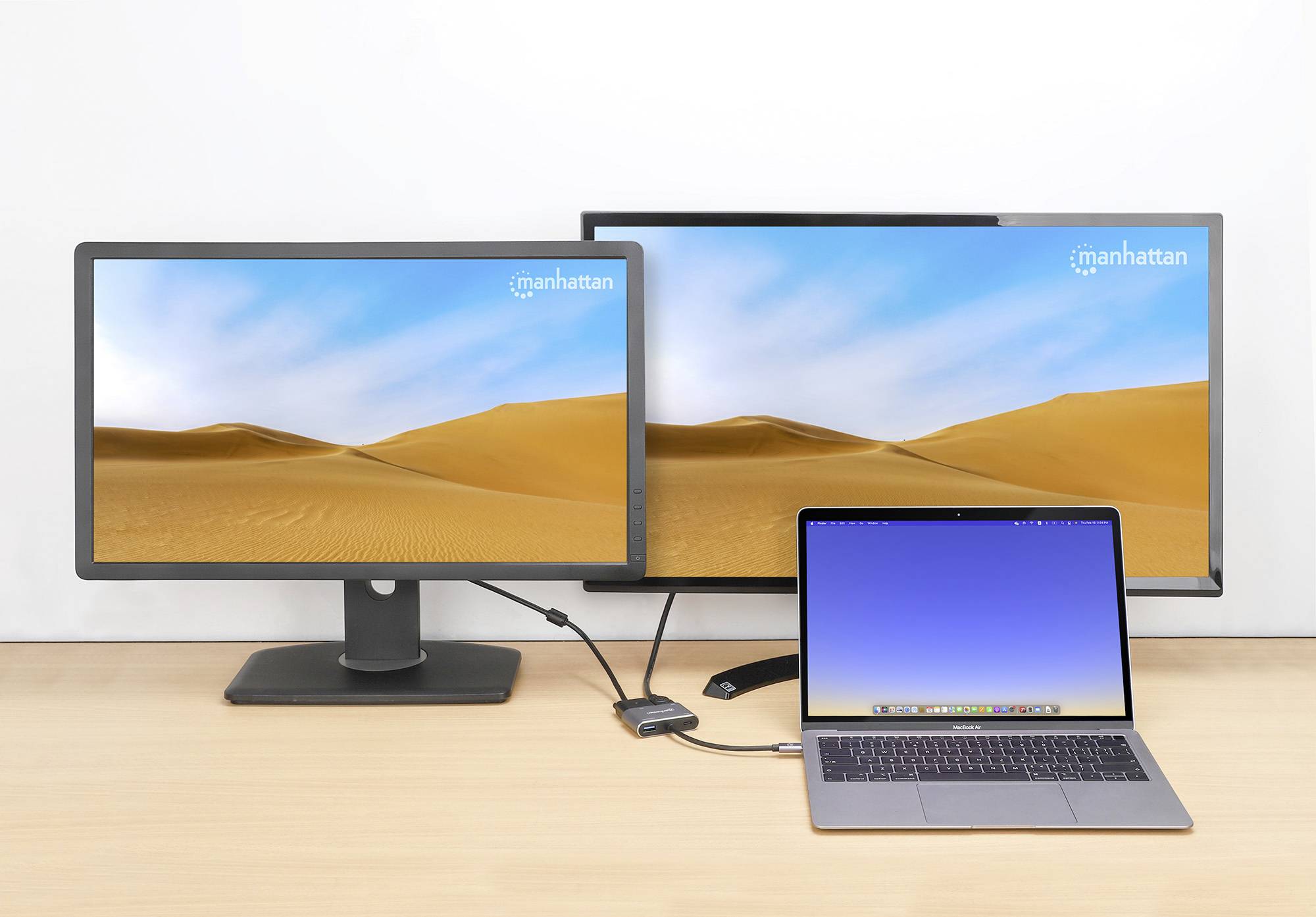 Twee computerbeeldschermen en een laptop op een tafel, allemaal met woestijnachtergronden. De laptop is aangesloten via een kabel.