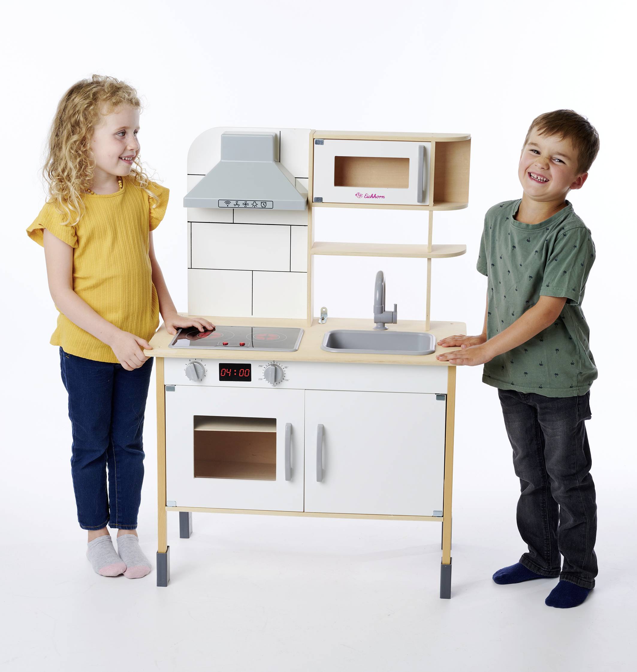 Twee kinderen spelen vrolijk met een houten speelkeuken, bestaande uit een fornuis, gootsteen en kasten. Het meisje draagt een geel shirt.