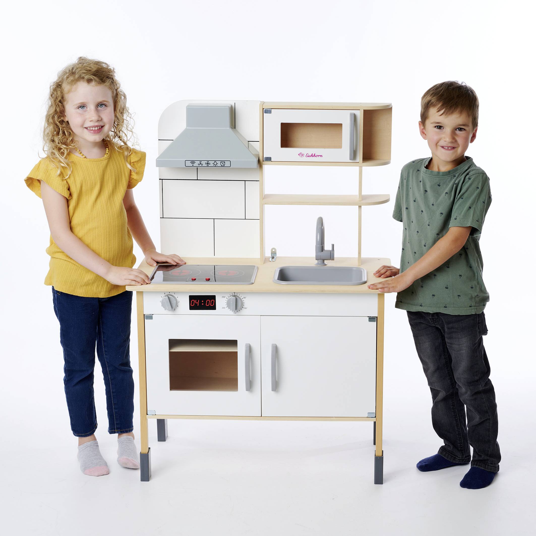 Een meisje en een jongen staan naast een houten speelkeuken. Het meisje draagt een geel bovenkleding, de jongen een groen gestippeld shirt. Beiden glimlachen.