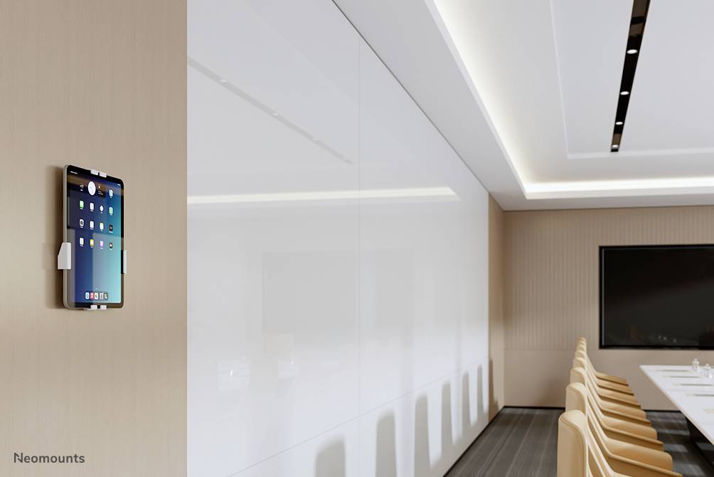 Tablet aan de muur in een moderne vergaderzaal, met een lange tafel en witte muren, links hangt een tablet.