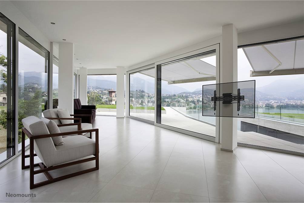 Een lichte, moderne ruimte met grote ramen biedt uitzicht op een schilderachtig landschap. Twee witte fauteuils staan links in de ruimte.