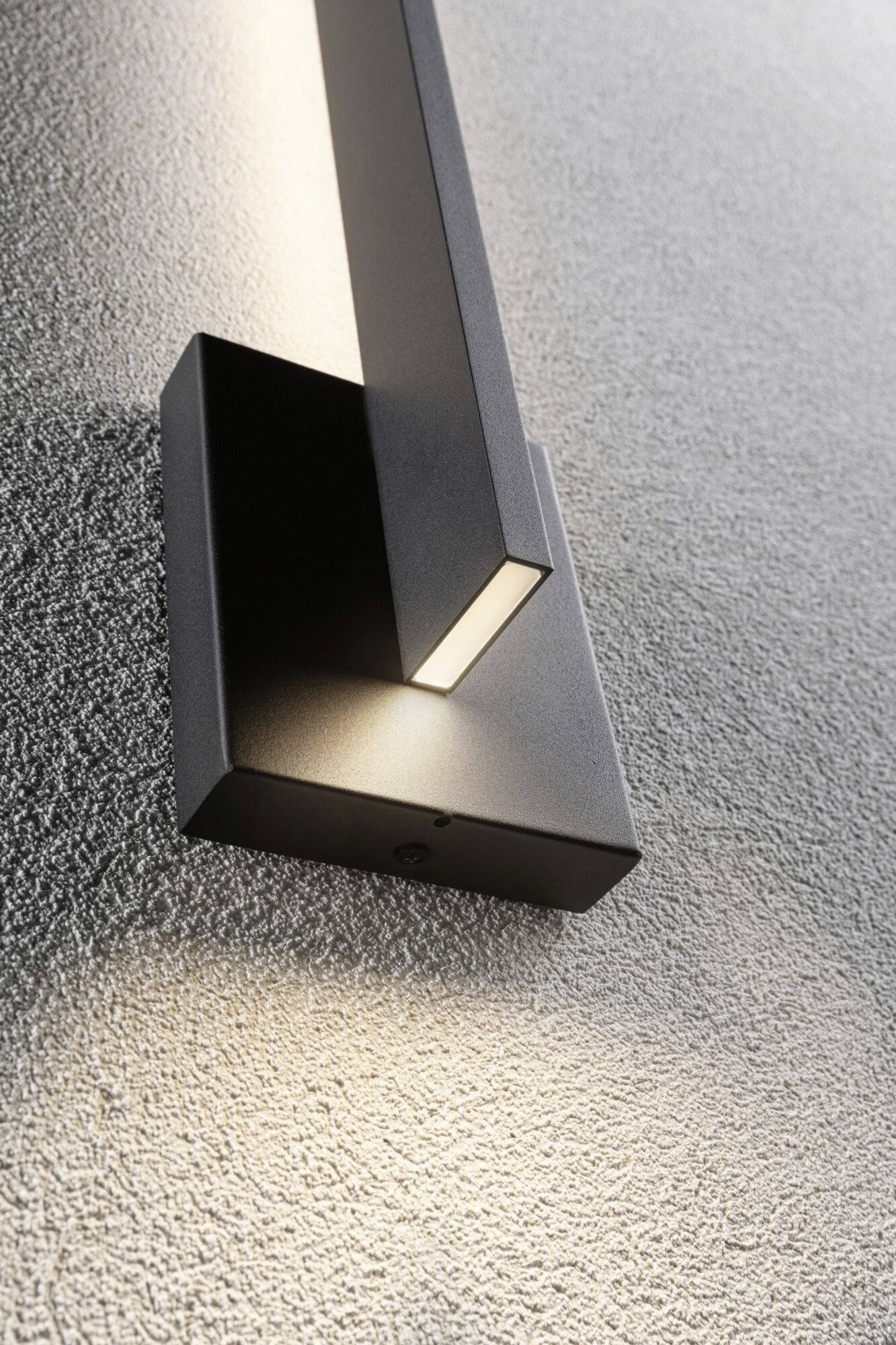 Moderne, zwarte wandlamp met geometrisch design, straalt zacht licht naar boven en beneden op ruwe, gestructureerde muur.