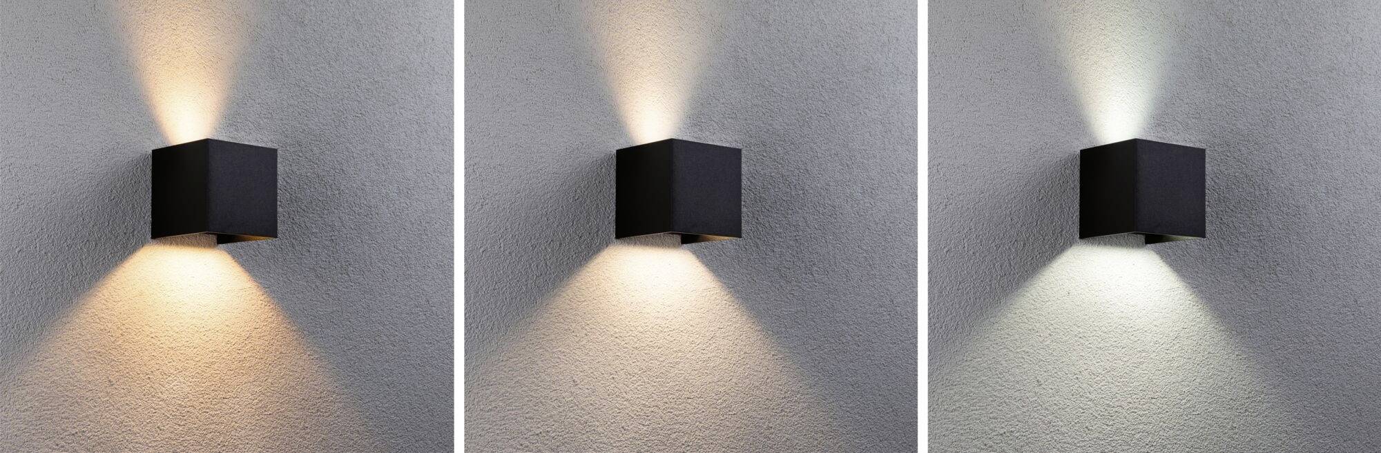 Drie zwarte kubische wandlampen aan een grijze muur, tonen verschillende lichtskleuren: warm, neutraal en koud licht.