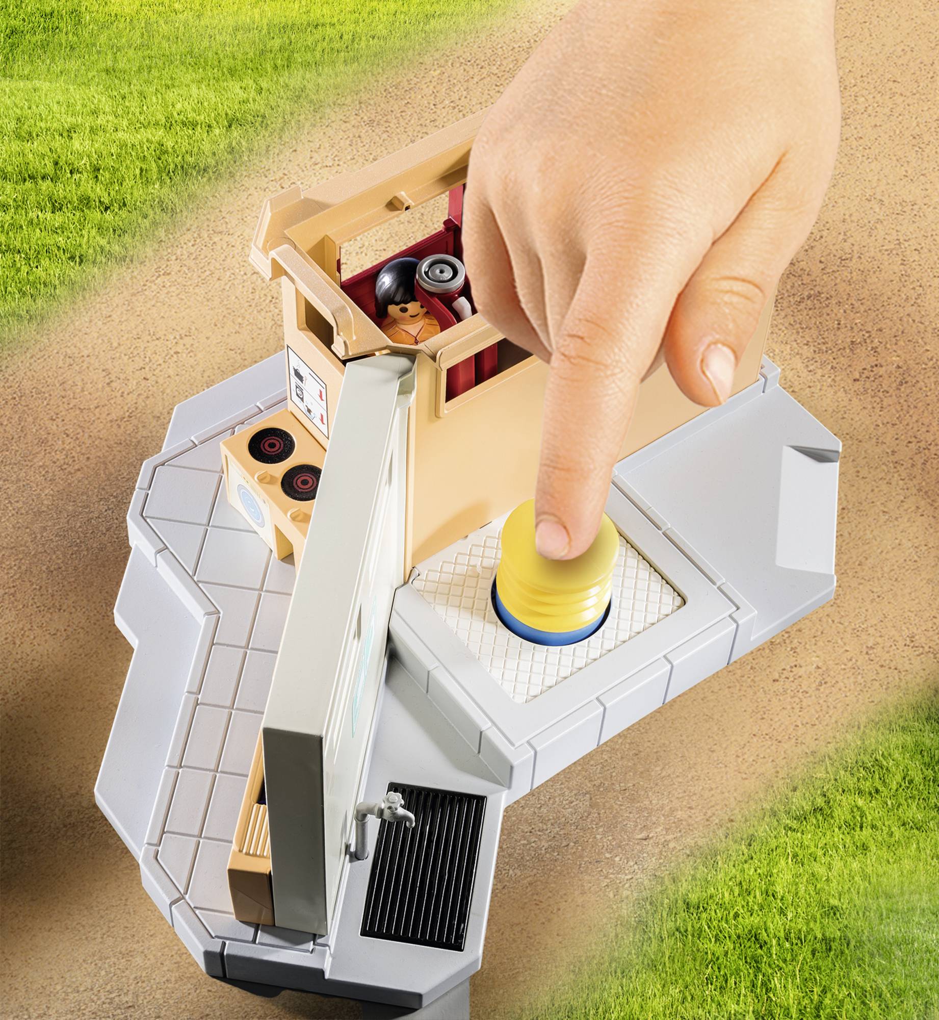 Een vinger drukt op een gele knop op een speelgoed-bouwset die een scène toont met een speelgoedauto en een poppetje.