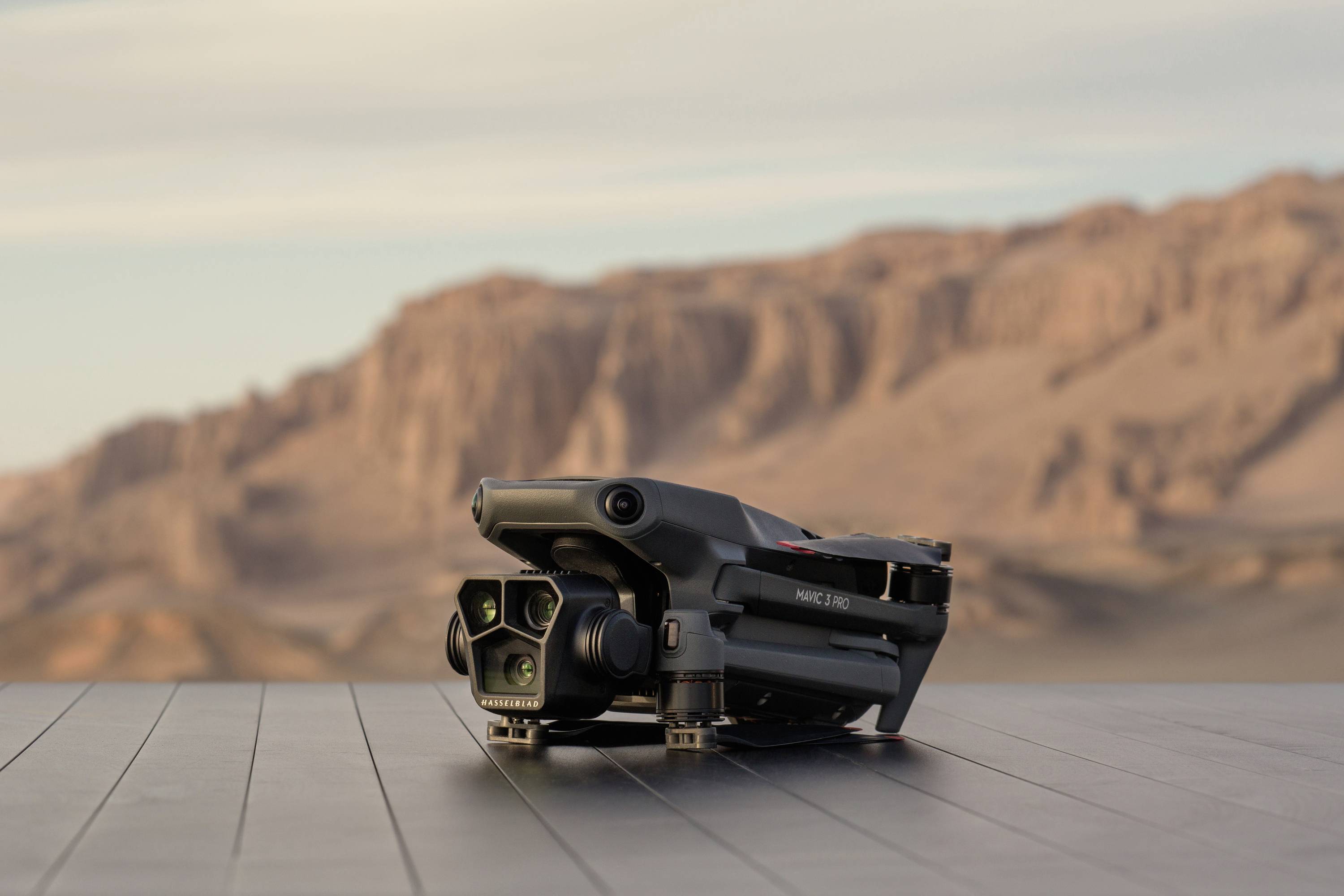 Een drone ligt op een houten tafel voor een woestijnlandschap met rotsachtige heuvels op de achtergrond.