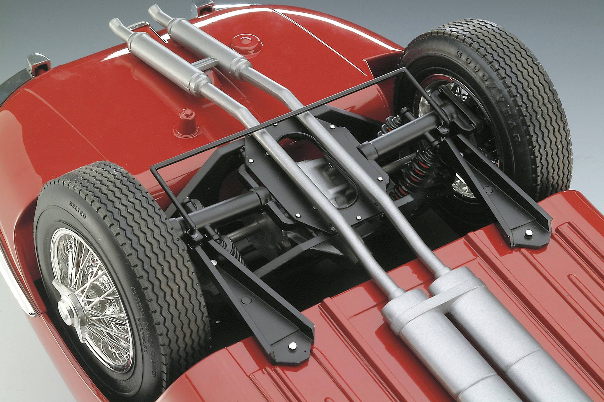 Rode carrosserie van een oldtimer van onderen, toont de wielophanging, de uitlaat en details van de achteras.