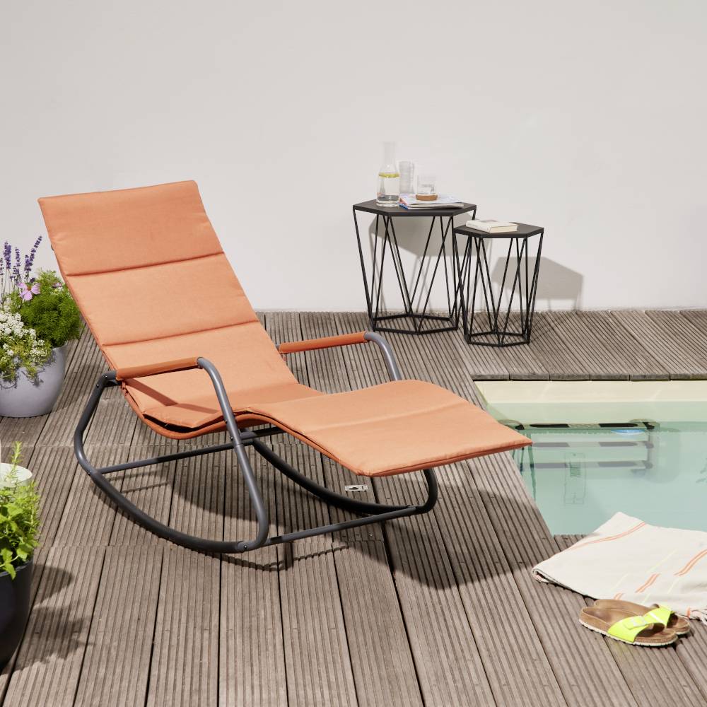 Een oranje schommelstoel staat naast een zwembad op een houten terras. Op de achtergrond zijn planten en een kleine tafel met dranken.
