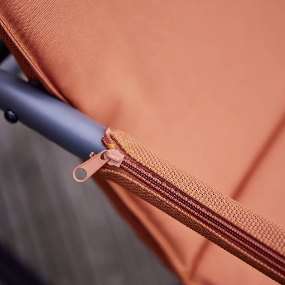 Close-upfoto van een oranje stof met een rits en een zwart metalen frame, mogelijk onderdeel van een tuinmeubel.