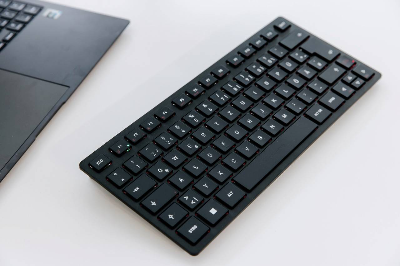 Zwarte draadloze computertastatur naast een laptop op een witte tafel. De toetsen zijn gerangschikt in een QWERTZ-indeling.